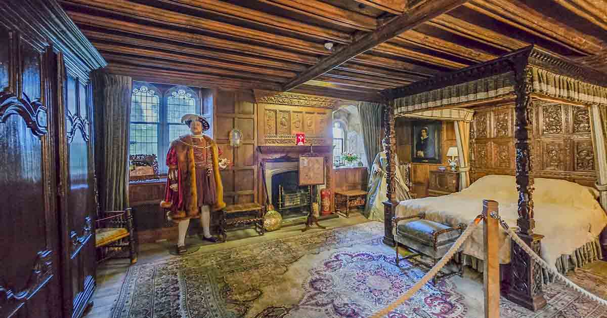 Anne Boleyn Dark wood four-poster bed within an orange room, adorned with portraits.