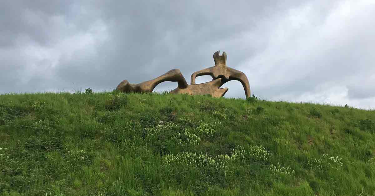 Henry Moore Sculpture Massive abstract bronze figure atop a grassy mound.