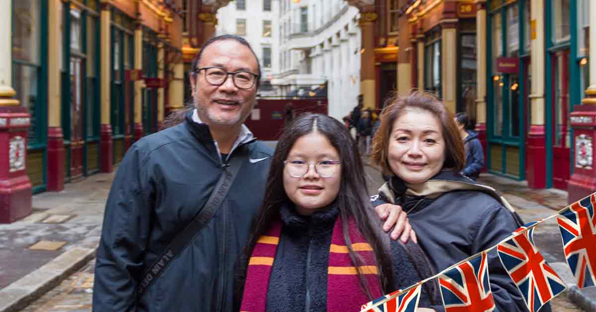 Young girl in Harry Potter scarf with parents in front of ornate Victorian architecture.