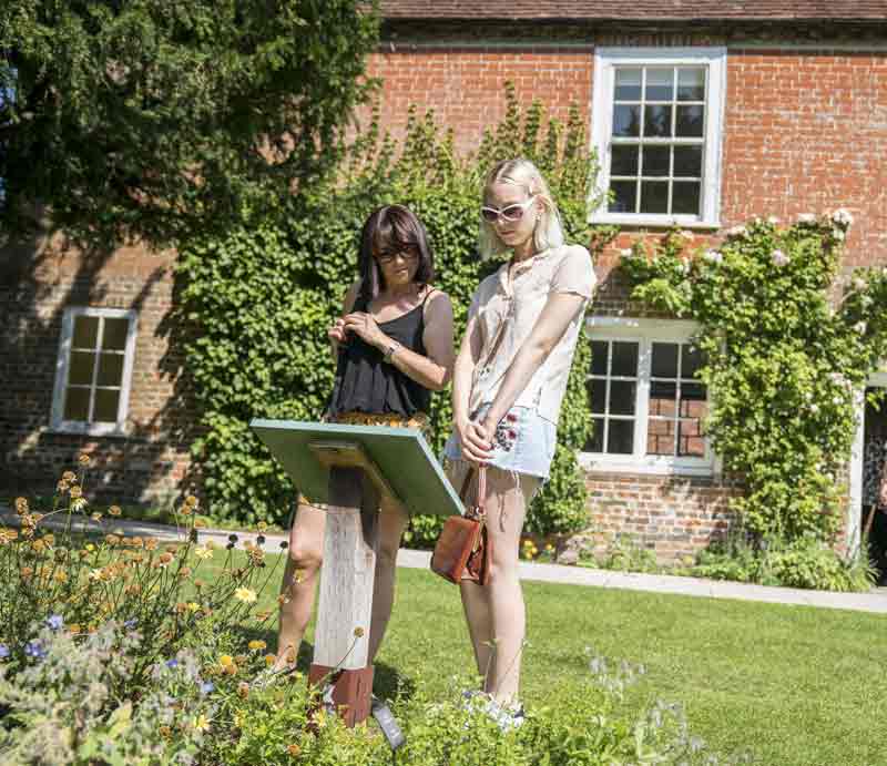 Building exterior with visitors reading an information sign in the garden.