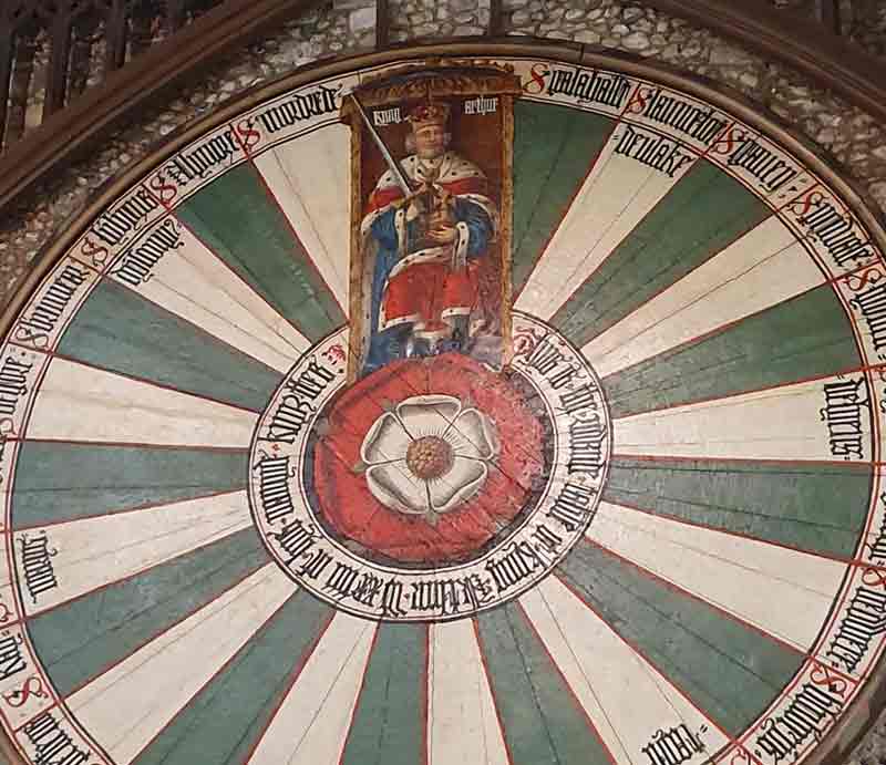 King Arthur Radiating outwards from a central red and white Tudor rose alternating stripes of white and green below a portrait of an enthroned king in ceremonial robes.