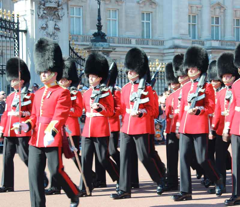 In red uniform and busby hat parading outside Buckingham Palace.