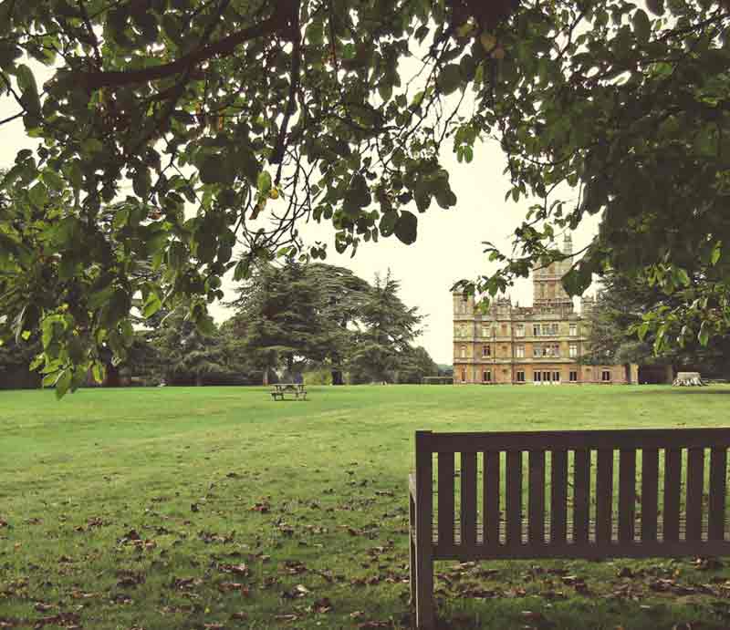 Wooden bench in gardens with the building in the distance.