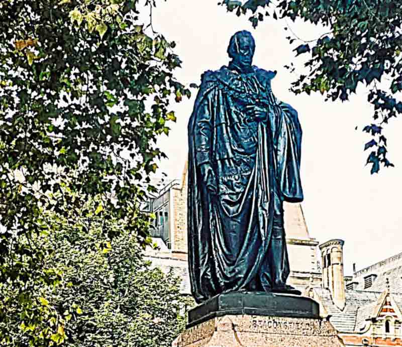 Dressed in his robes as 1st Earl of Beaconsfield, standing on a red granite pedestal.