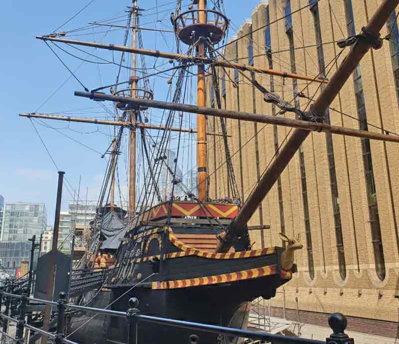 Black hull decorated with yellow and red trim with tall wooden masts and rigging.