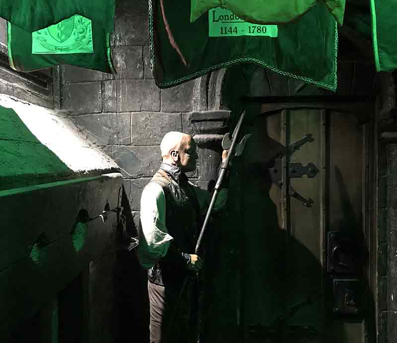 Guard with axe outside stone cell with eerie green light.