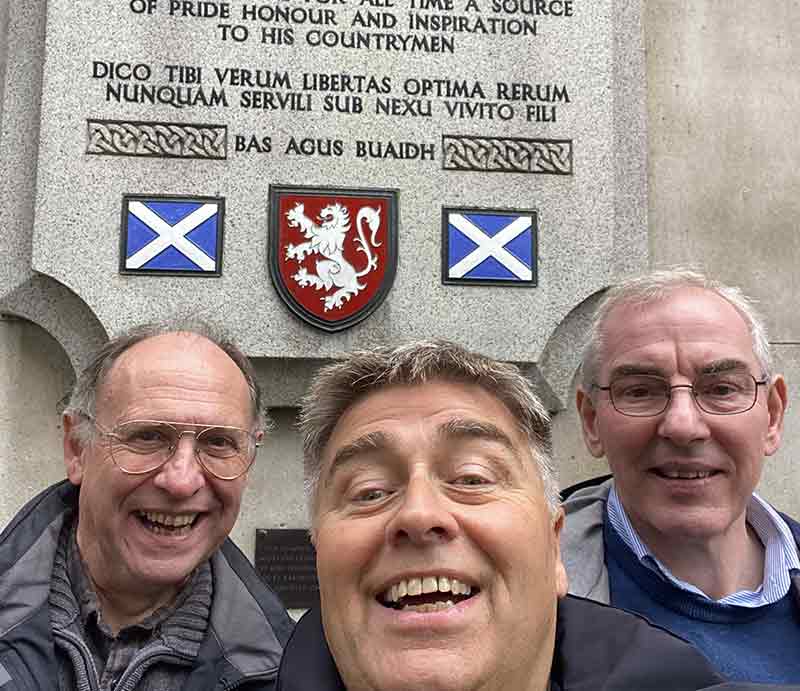 Rob and guests in front of stone plaque with Scottish flags and lion rampant.