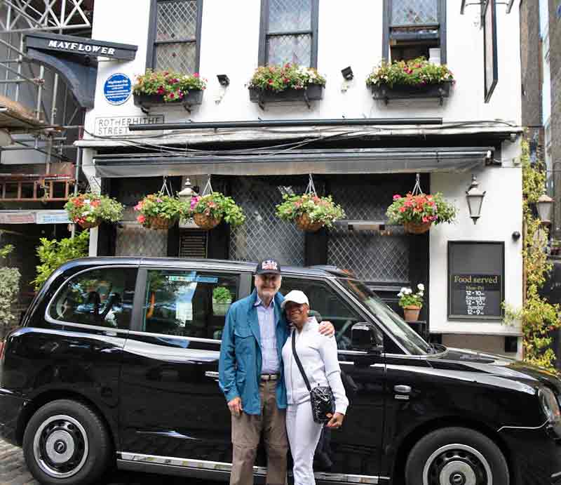 Guests by taxi outside pub with hanging flower baskets.