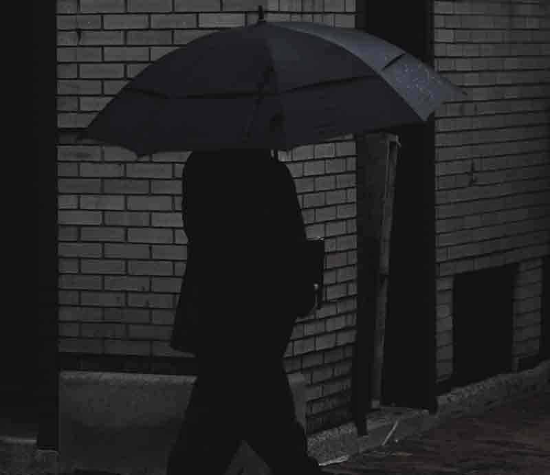 In shadows carrying umbrella.