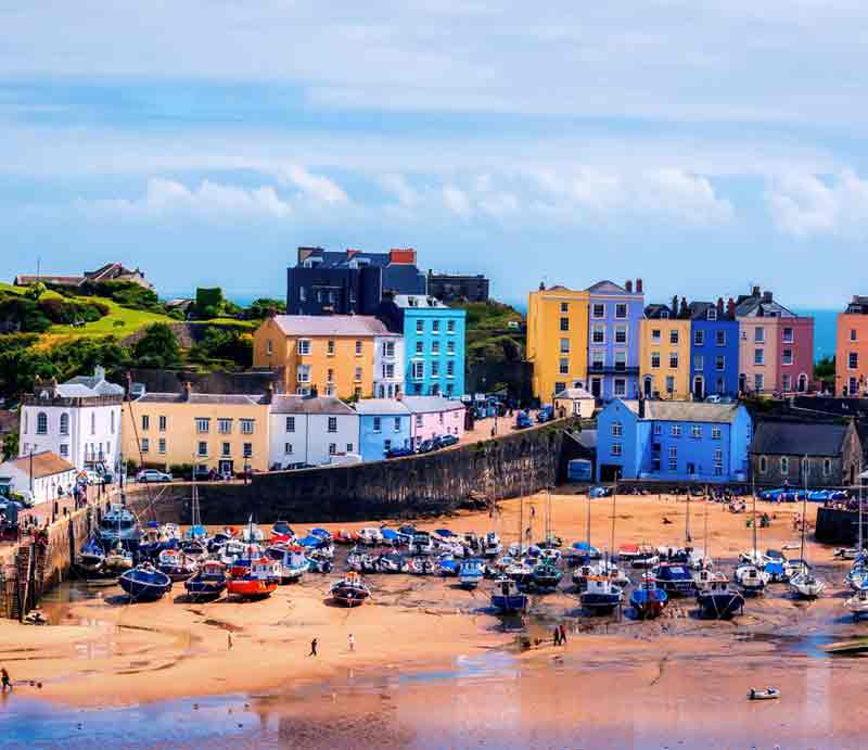 Tenby Harbour at low tide with fishing boats and brightly painted cottages.